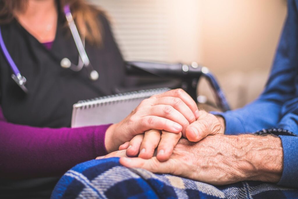 Pflegerin im Hospiz hält die Hand eines Patienten